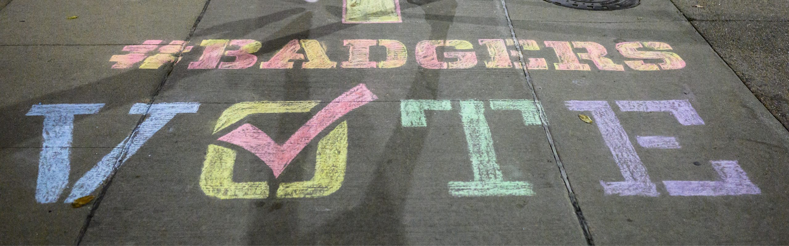 Sidewalk chalking reads in rainbow colors reads "#BADGERS VOTE"