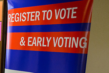 Photo of a banner with a blue background and white text on red stripes that reads Register to vote and early voting.