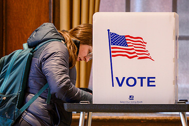Photo of a student standing at a voting booth and filling out a ballot on Election Day.