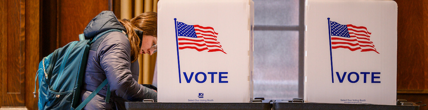 Photo of a student standing at a voting booth and filling out a ballot on Election Day.