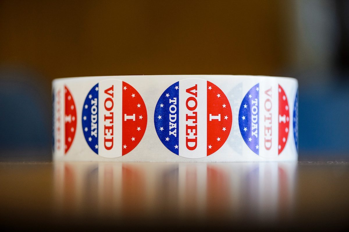 Photo of a roll of stickers sitting on a table. The round stickers are red, white and blue and display the words I voted today.