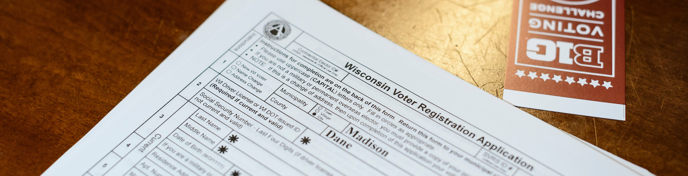 Photo of a Wisconsin voter registration application form sitting on a table next to a bookmark with the words Big Ten Voter Challenge.