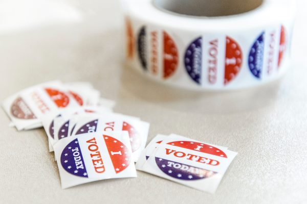 A roll of stickers sits on a table with individual stickers in a pile in front. The stickers read I voted today.